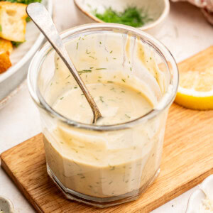 Tahini dill dressing in a glass jar with a serving spoon.