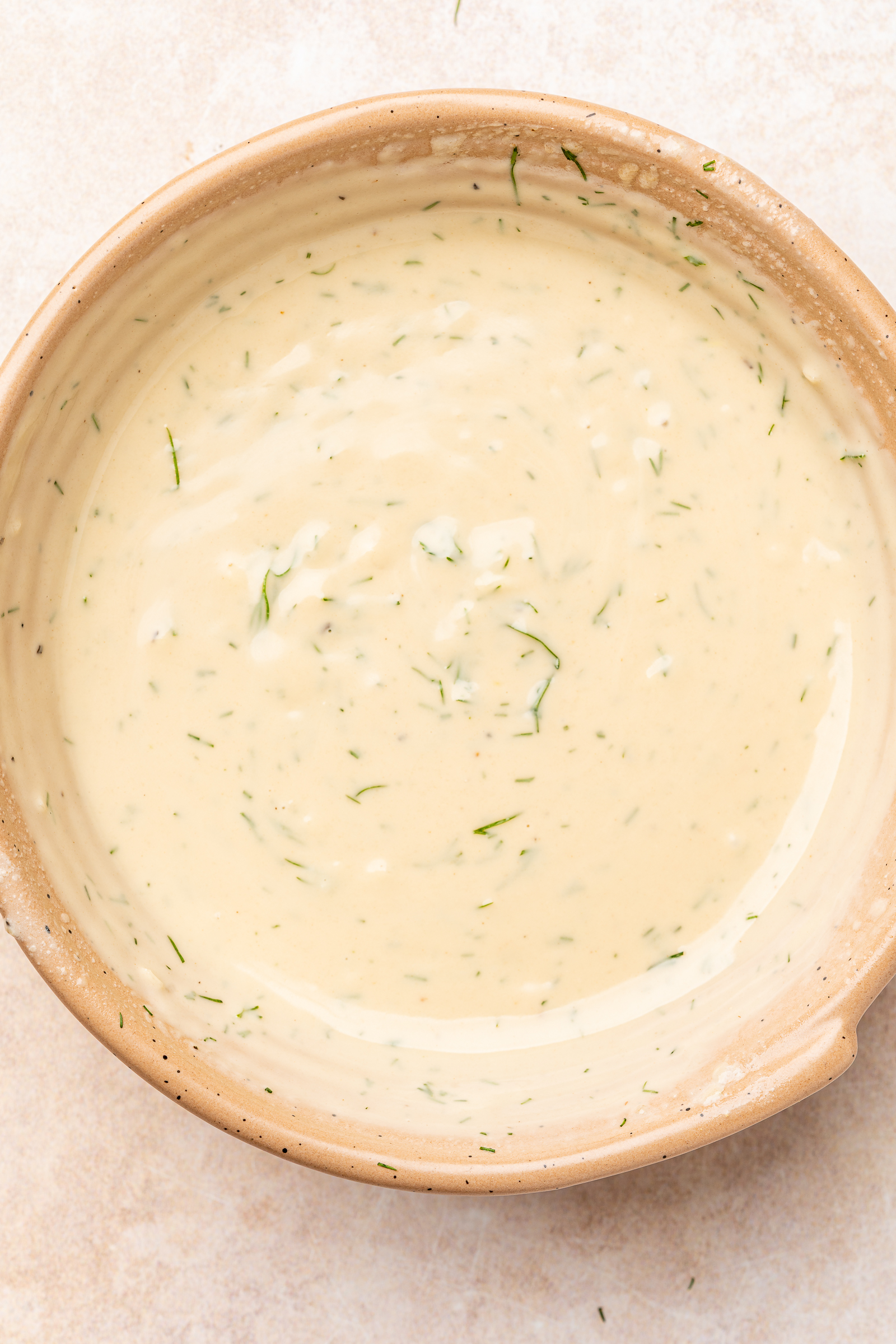 Dill being added to bowl with tahini dressing.