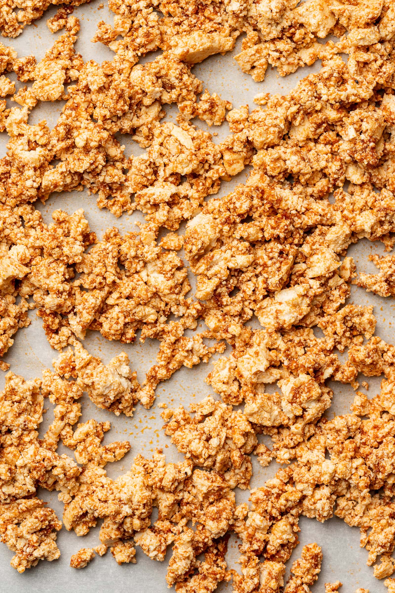 Crumbled seasoned tofu spread evenly on to a parchment lined baking sheet.