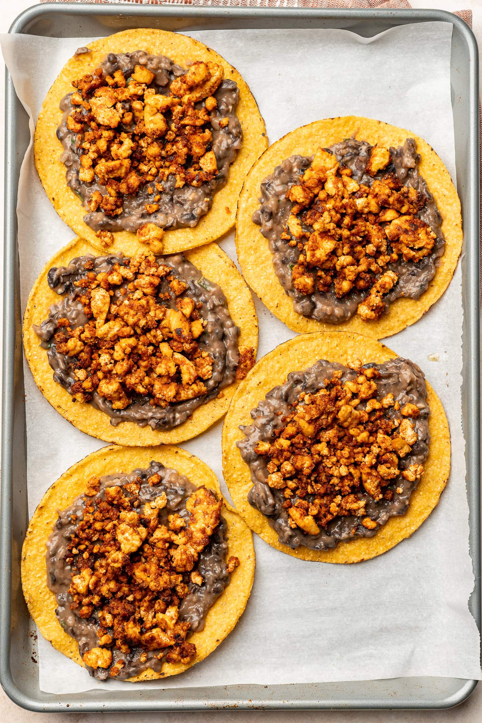 Tofu crumbles being put on top of the beans on the tostada shells.