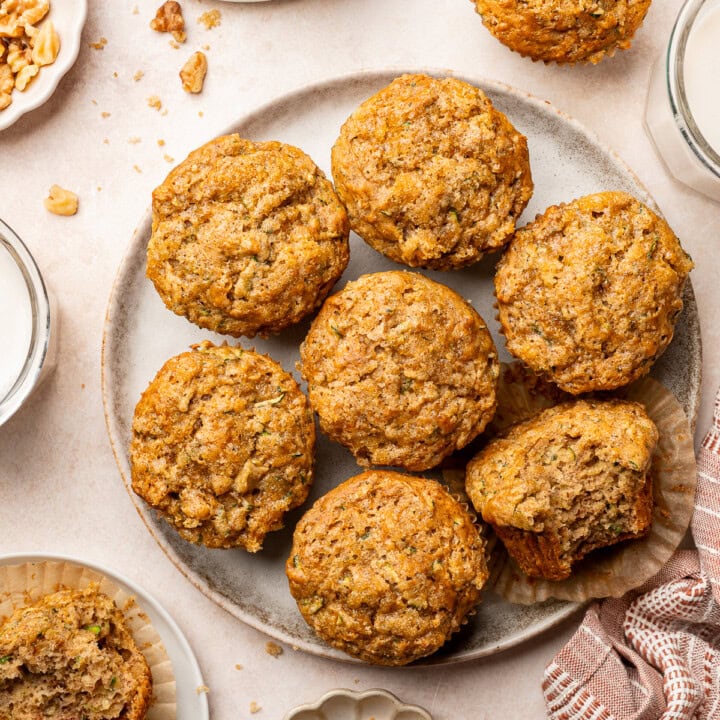 Banana zucchini muffins on a serving plate, one with bite taken out.