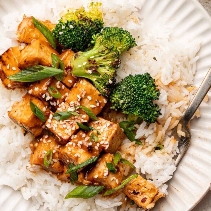 Miso glazed tofu on top of a bed of rice with charred broccoli, sesame seeds, and green onions.