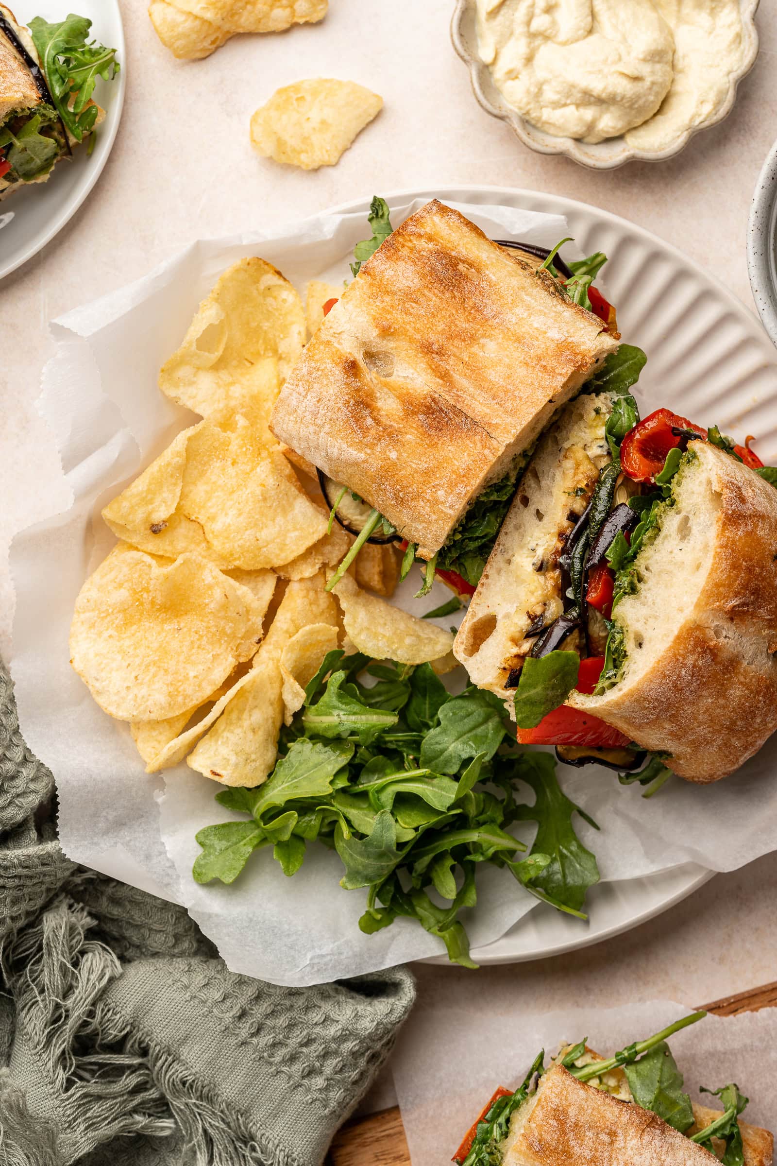 Roasted veggie sandwich cut in half on a serving plate with a side of chips.