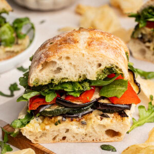 Roasted veggie sandwich cut in half on a wooden board.