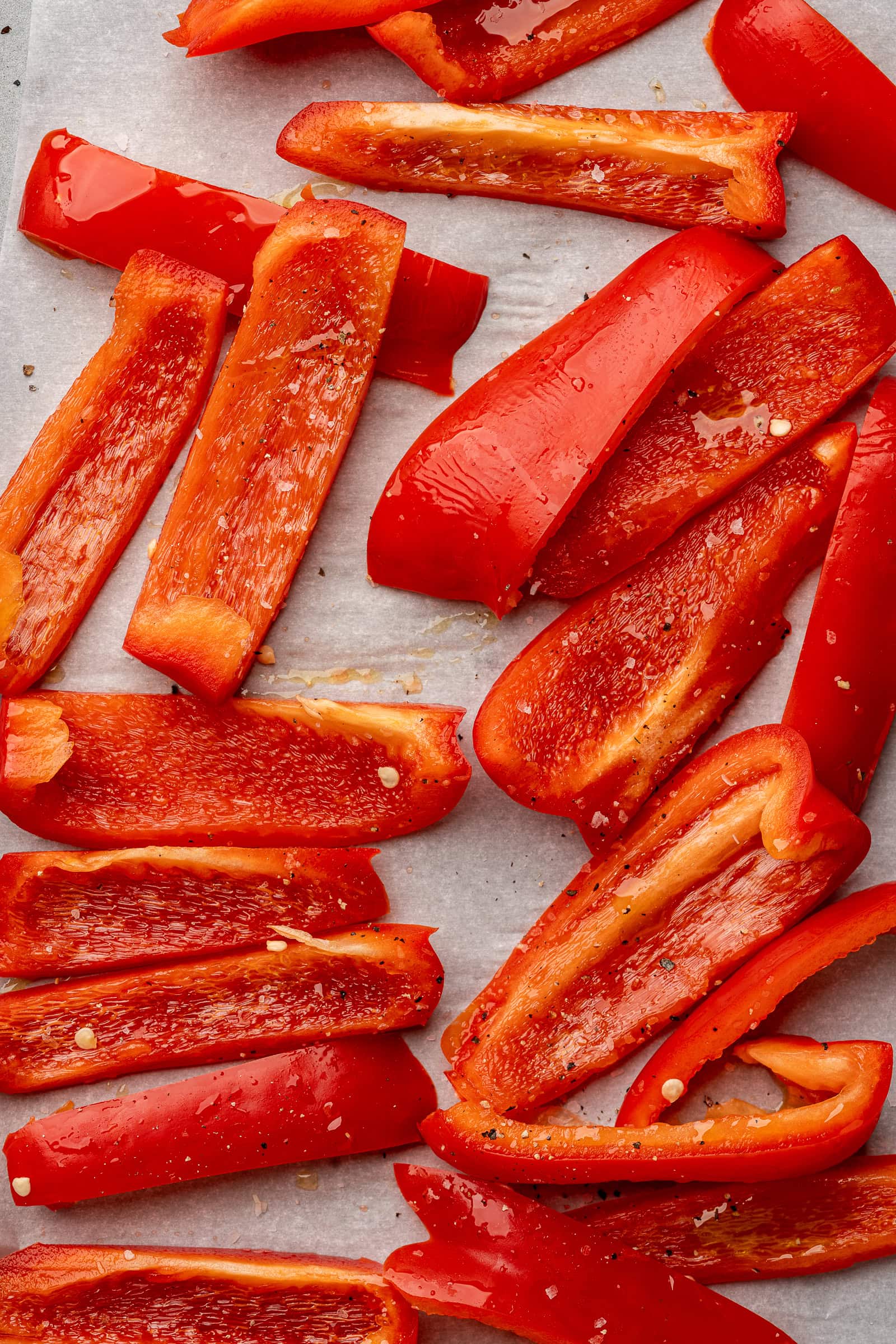Red bell peppers sliced on a parchment-lined baking sheet.