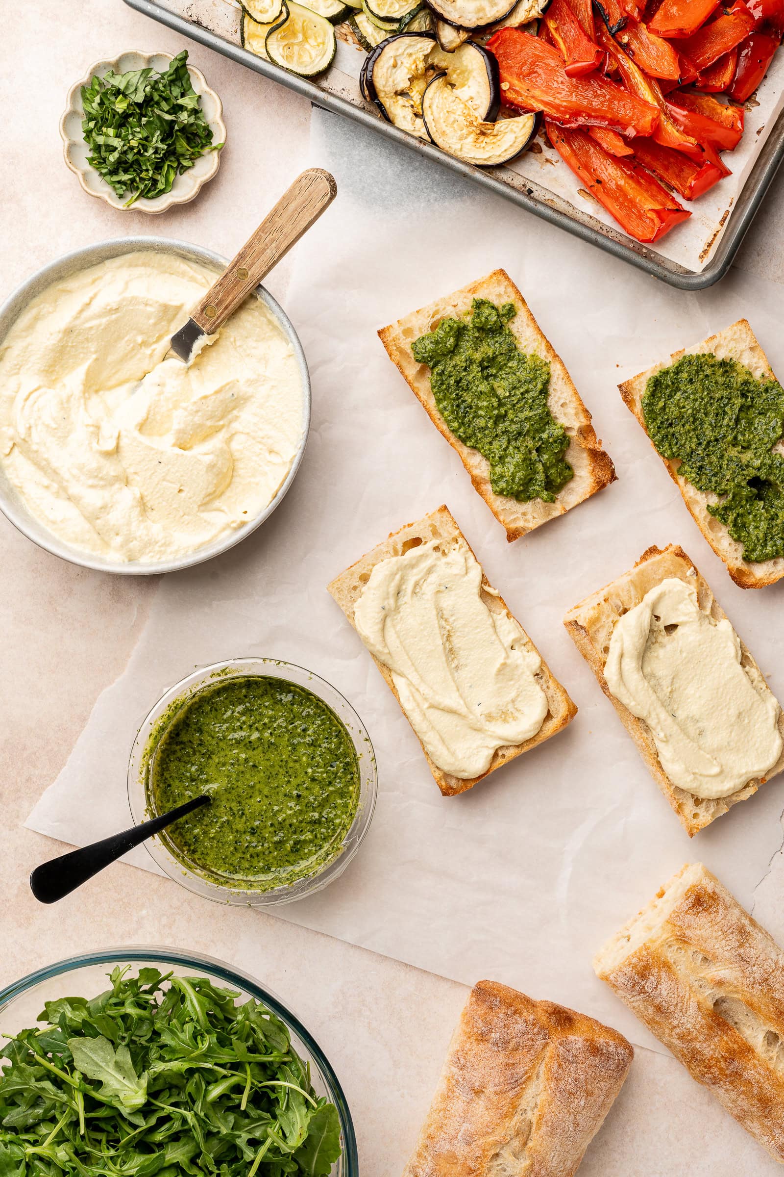 Vegetable sandwiches being built by spreading a layer of ricotta and pesto on each sides of the bread.