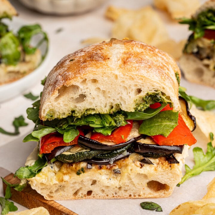 Roasted veggie sandwich cut in half on a wooden board.