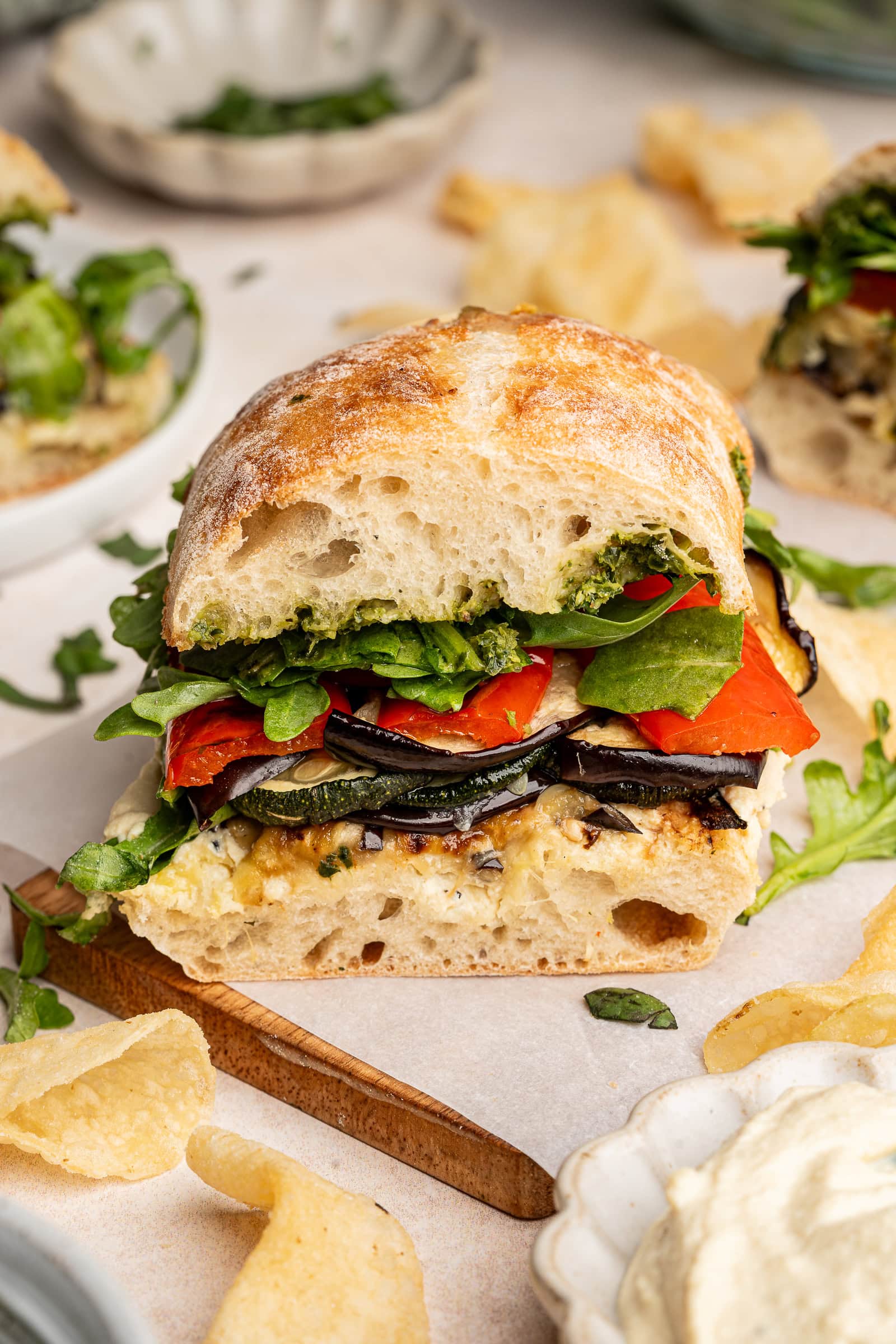 Roasted veggie sandwich cut in half on a wooden board.