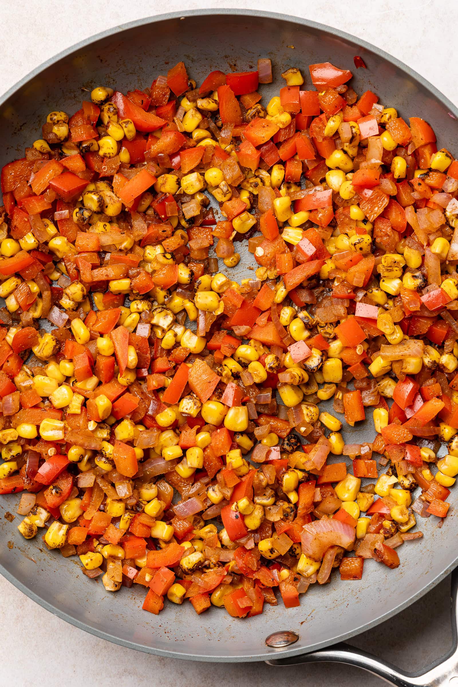 Onion, red bell pepper, and charred corn in a pan after sautéing.