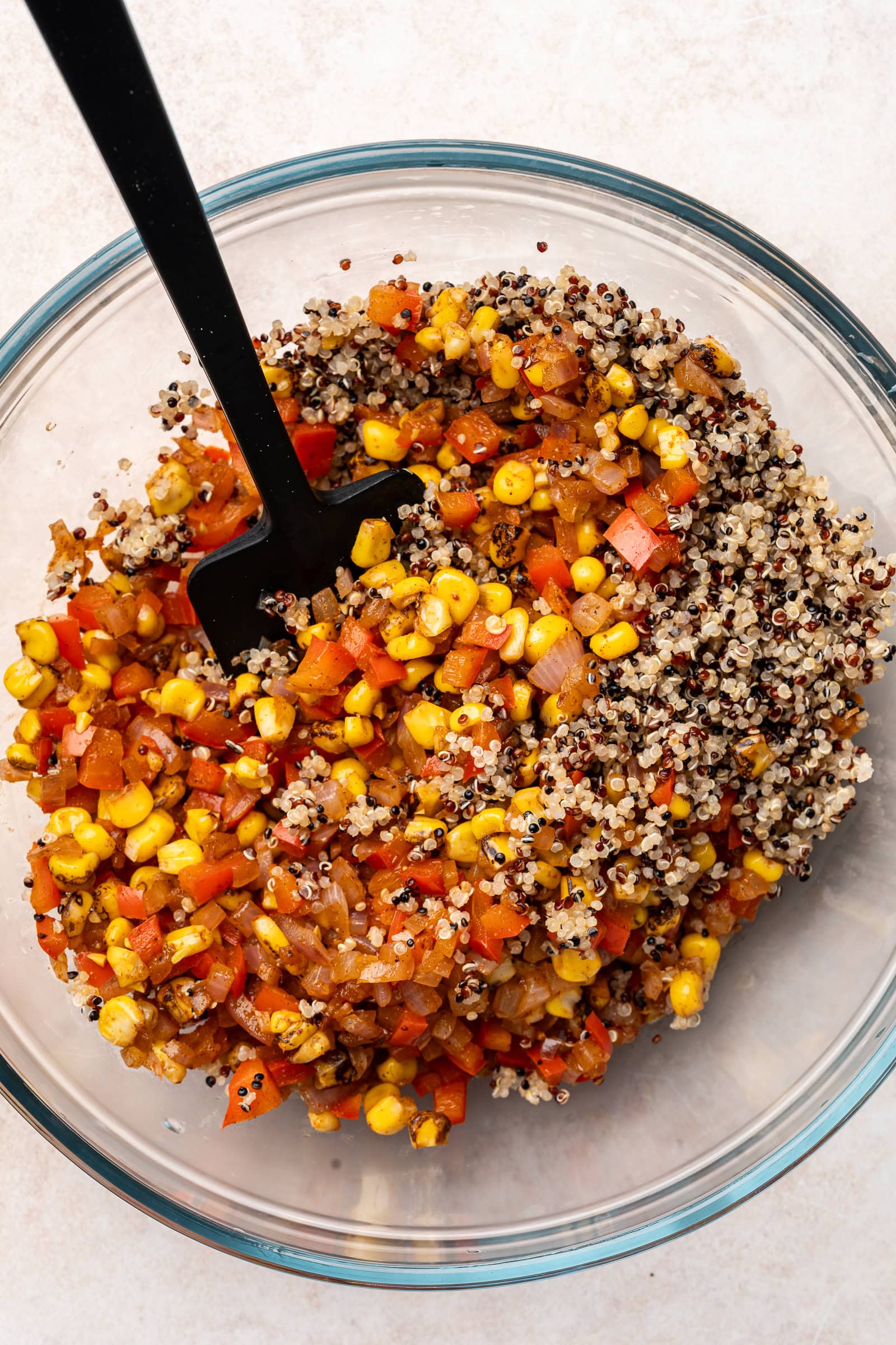 Corn mixture and quinoa being mixed together in a large glass bowl.