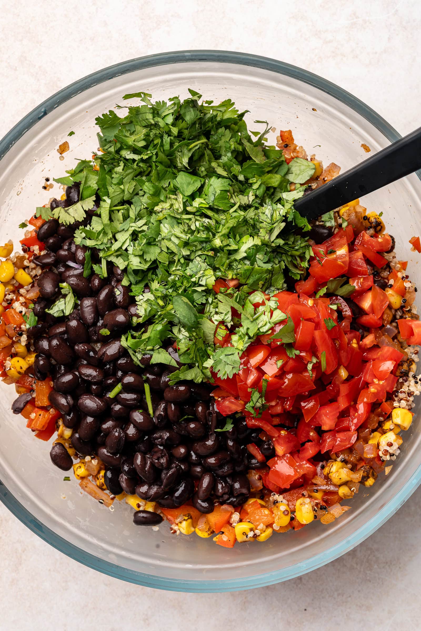 Black beans, cherry tomatoes, and cilantro being added to quinoa mixture.