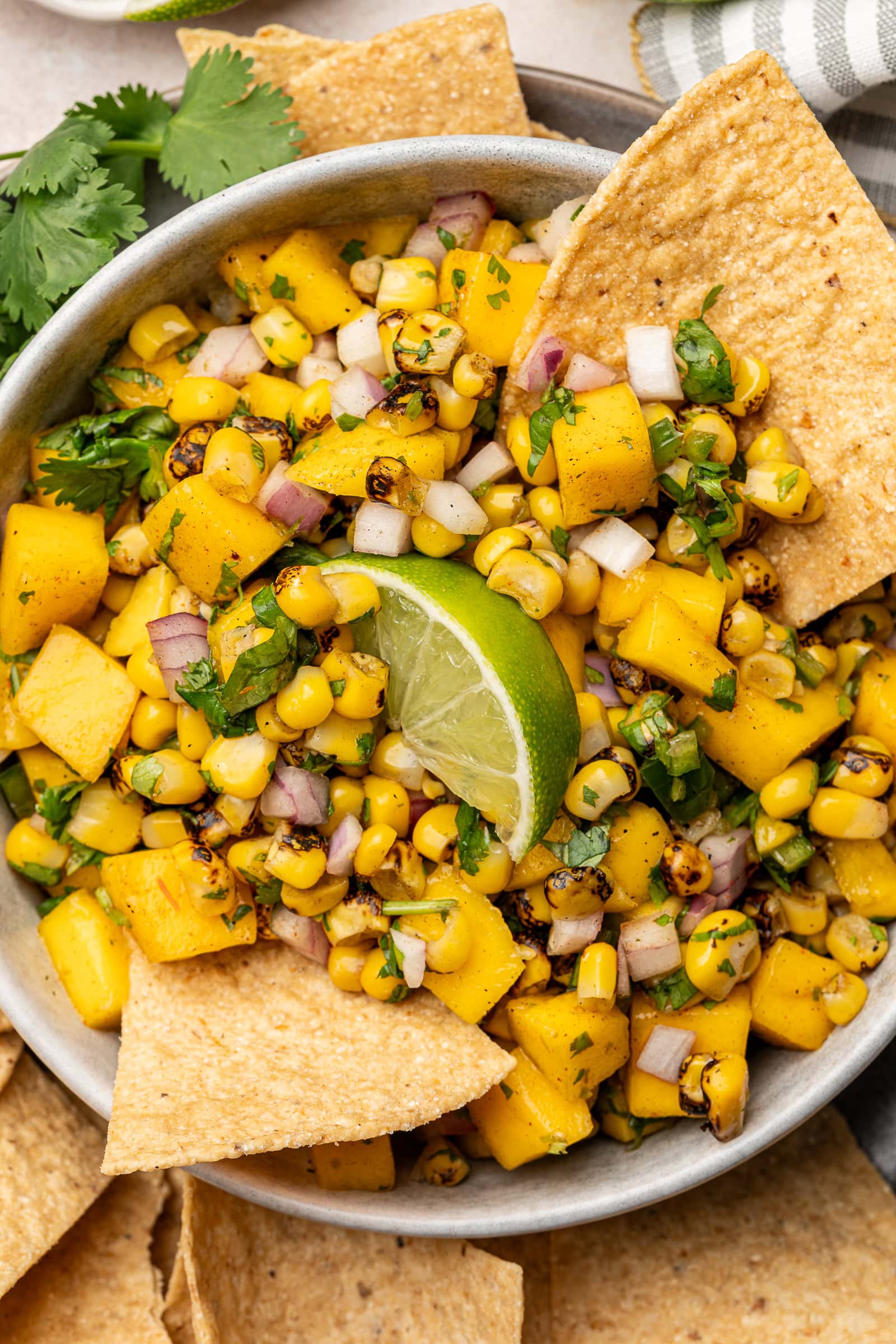 Corn mango salsa in a serving dish with tortilla chips and a lime wedge garnish.