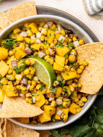 Corn mango salsa in a serving dish with tortilla chips and a lime wedge garnish.