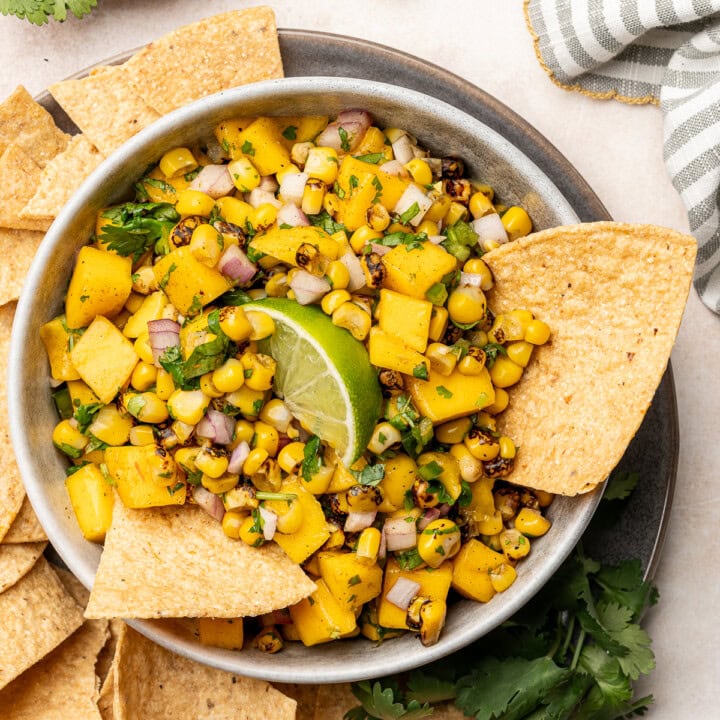 Corn mango salsa in a serving dish with tortilla chips and a lime wedge garnish.