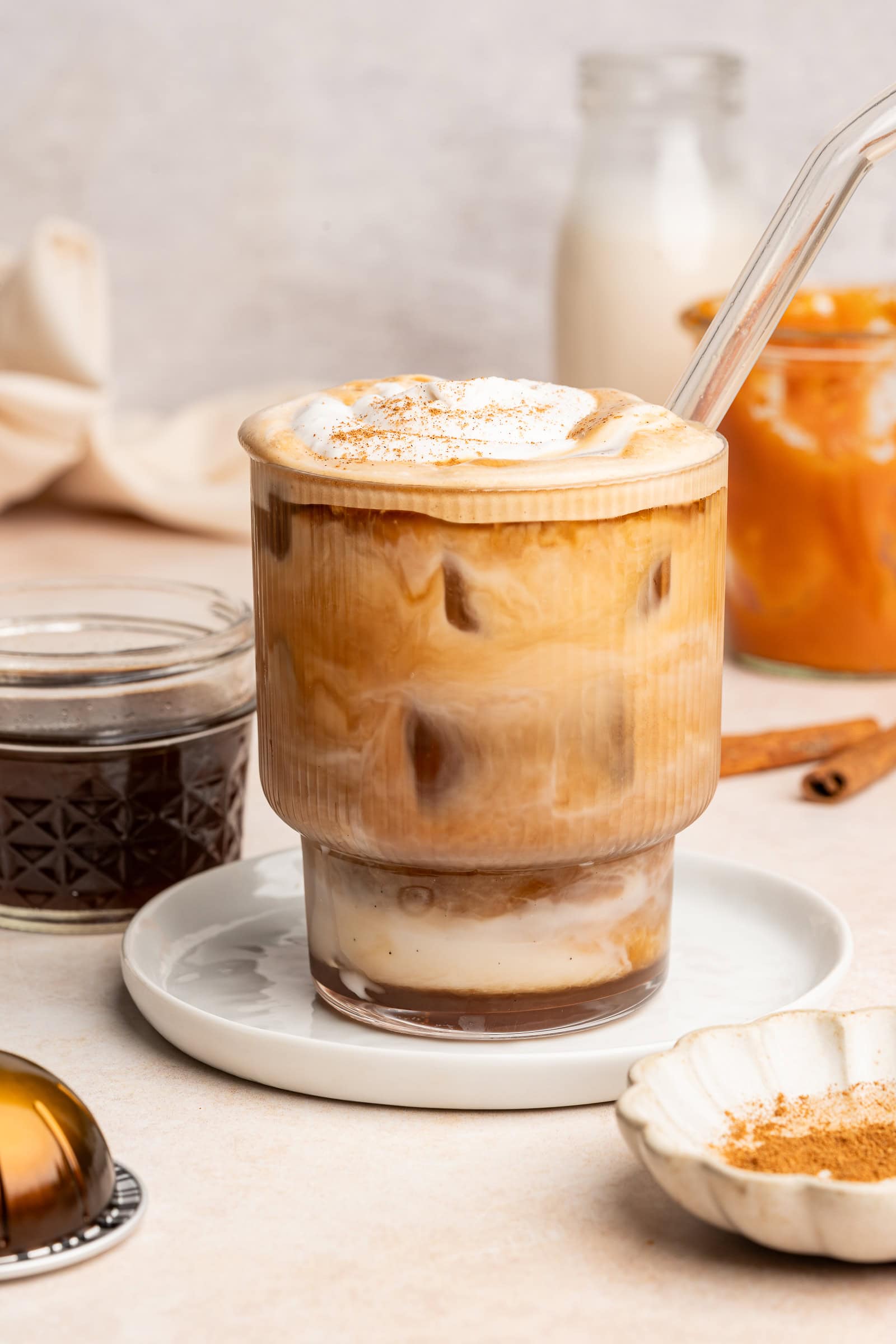 Pumpkin spice latte in a glass cup with a glass straw topped with whipped cream and pumpkin pie spice.