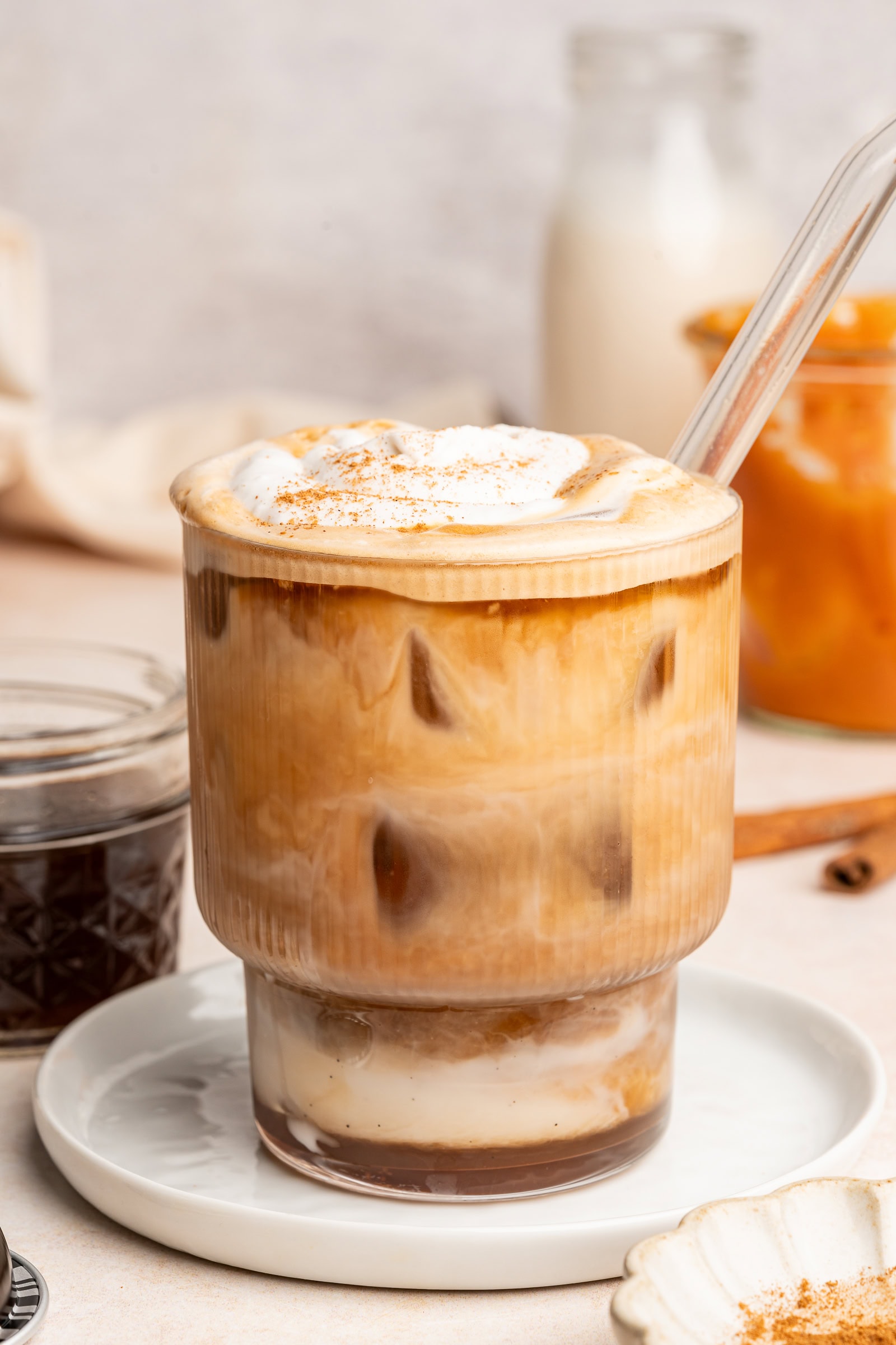 Pumpkin spice latte in a glass cup with a glass straw topped with whipped cream and pumpkin pie spice.