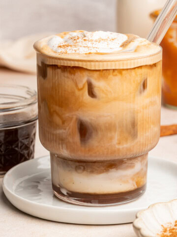 Pumpkin spice latte in a glass cup with a glass straw topped with whipped cream and pumpkin pie spice.