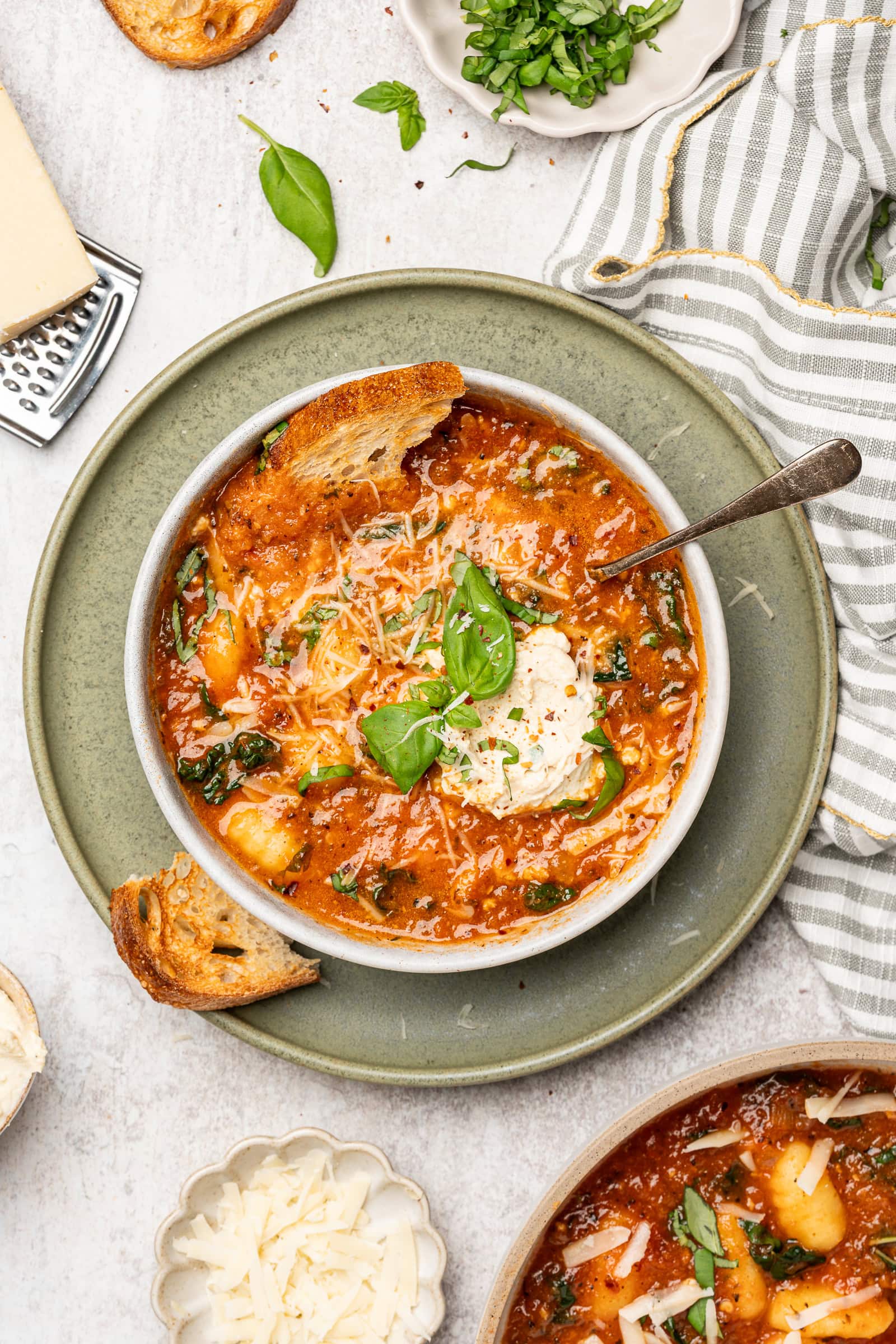 Tomato gnocchi soup in a bowl with crusty bread and topped with tofu ricotta and basil.