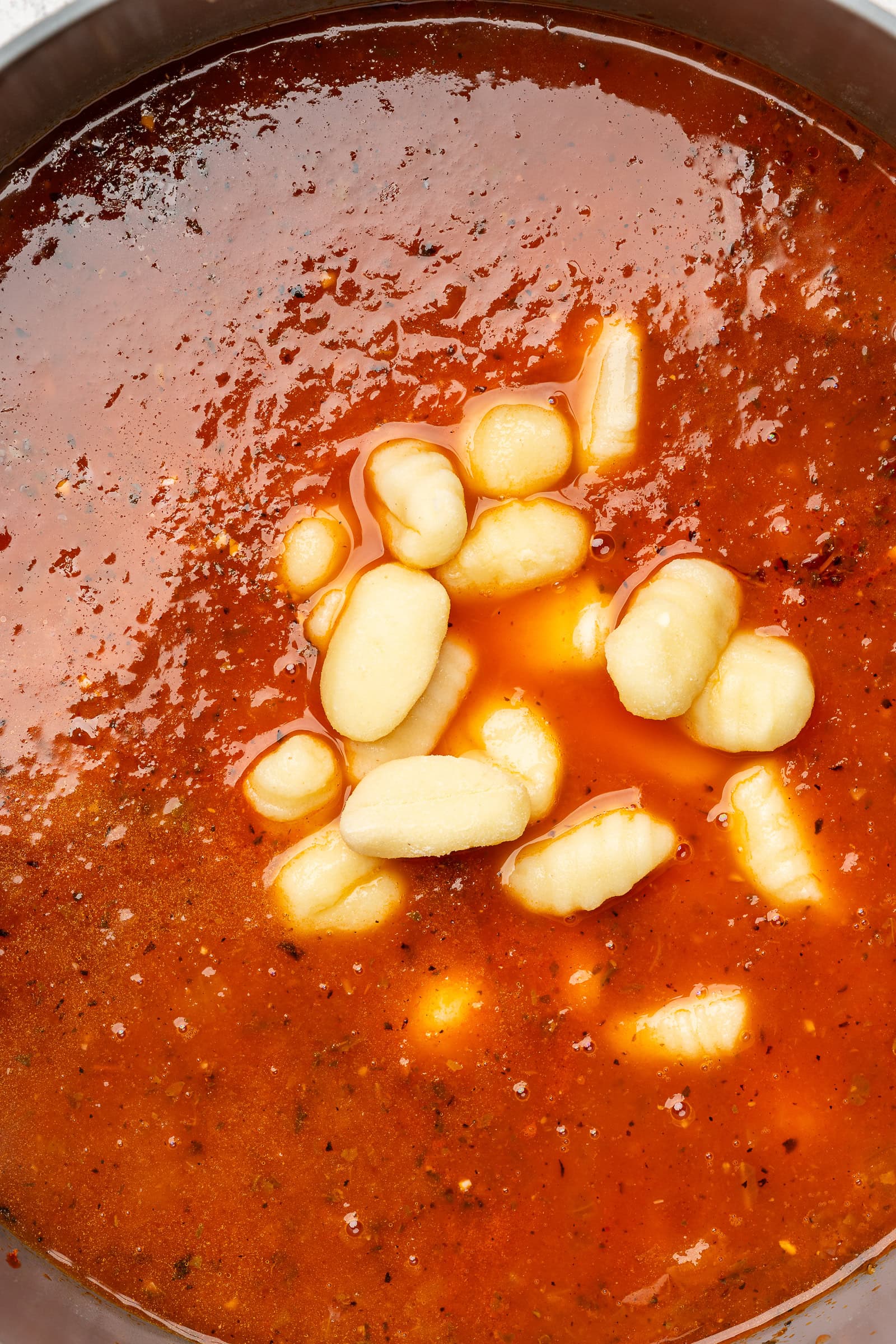 Uncooked gnocchi being added to a tomato broth in a large soup pot.