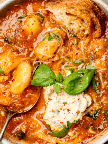 Tomato gnocchi soup in a bowl with crusty bread and topped with tofu ricotta and basil.