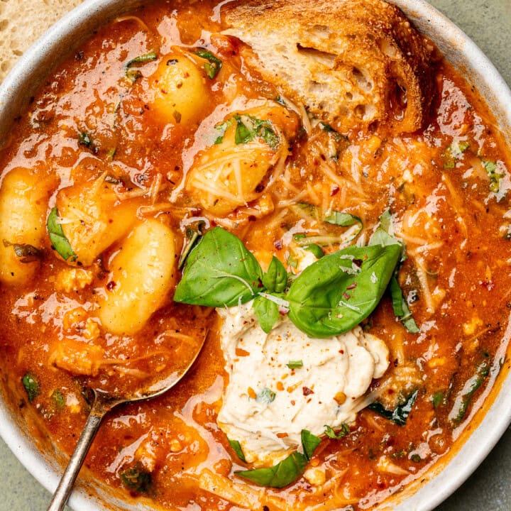 Tomato gnocchi soup in a bowl with crusty bread and topped with tofu ricotta and basil.