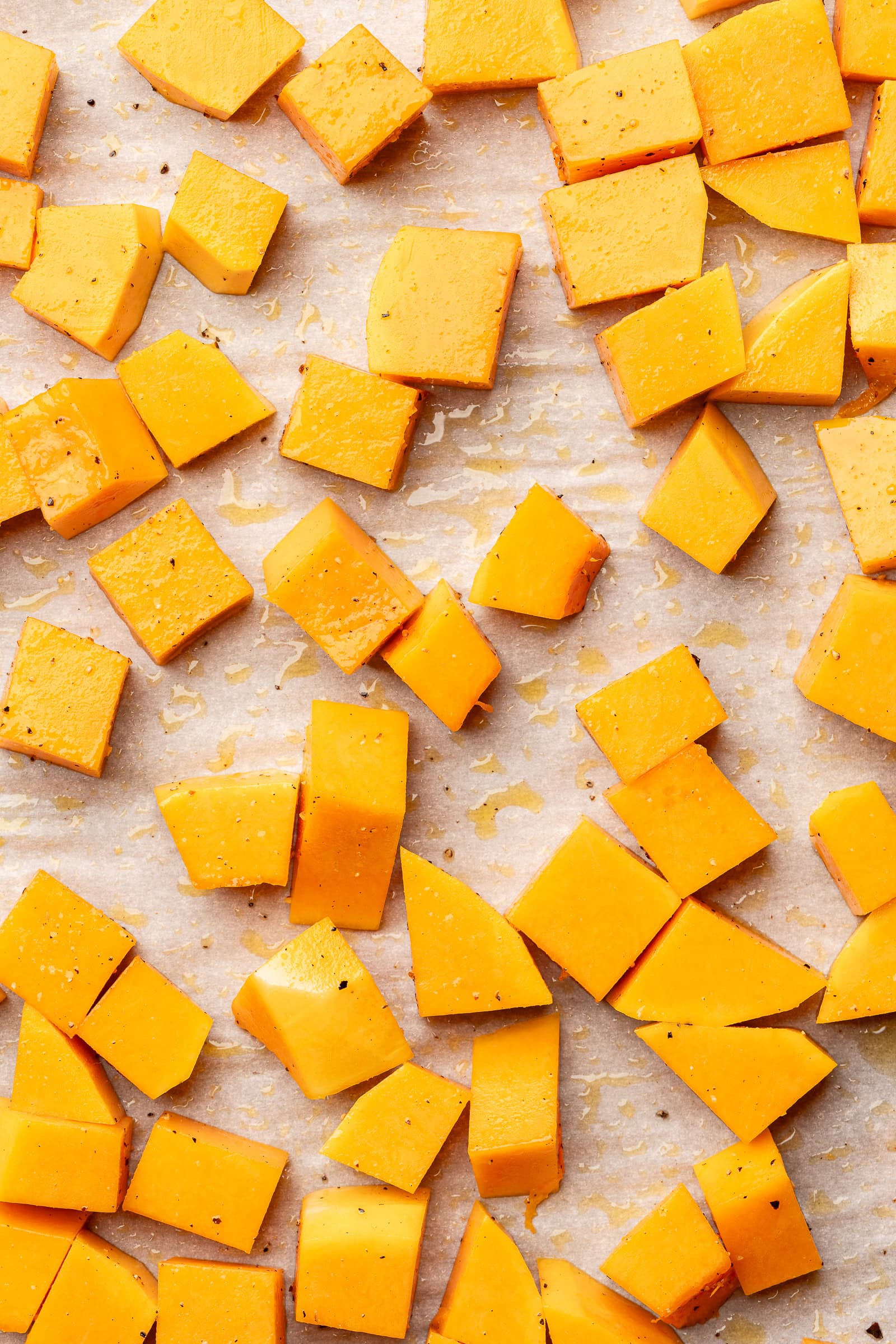 Raw cubed butternut squash on a parchment baking sheet.