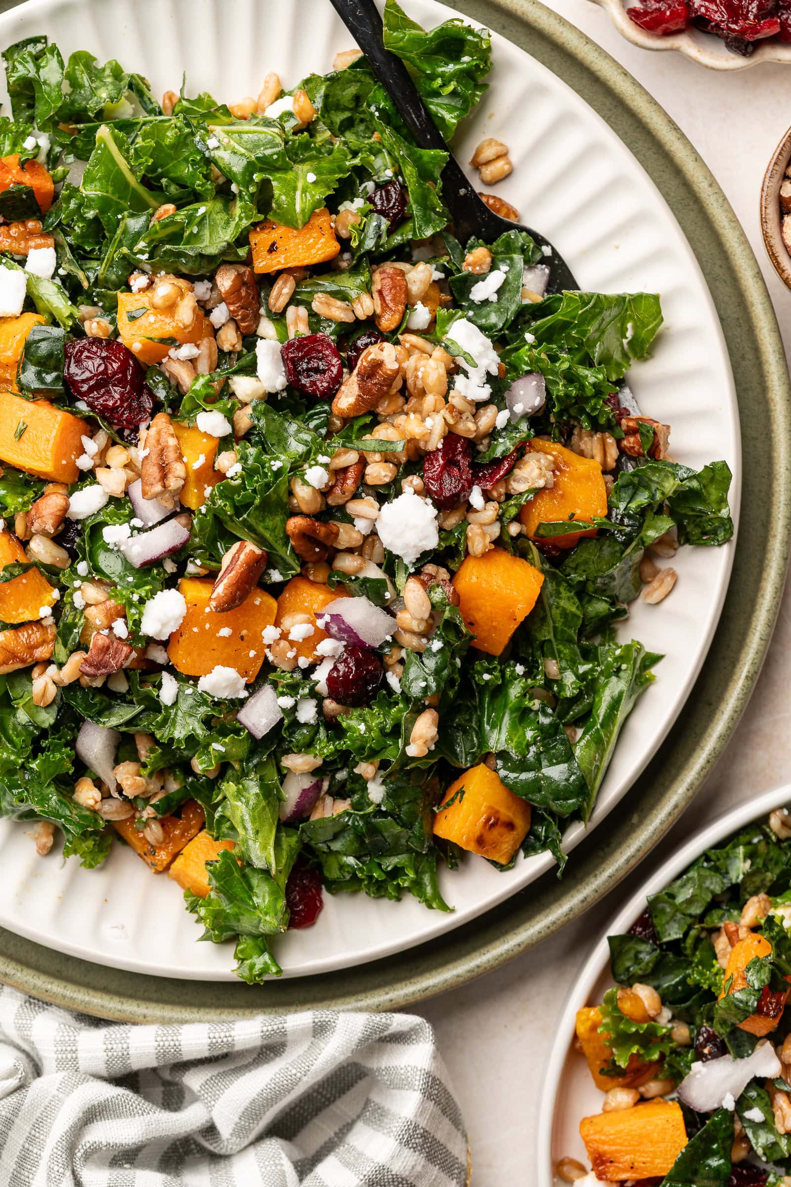 A serving plate of butternut squash kale salad topped with crumbled feta, red onion slices, and pecans.