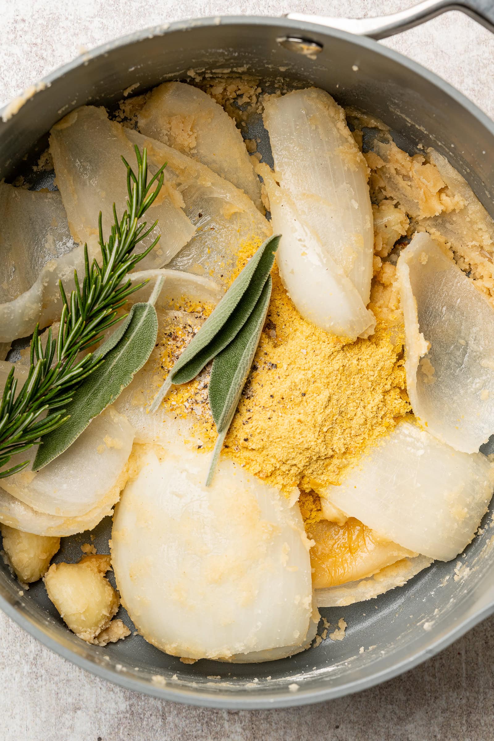 Flour mixed into the onions and garlic, and herbs and nutritional yeast being added.