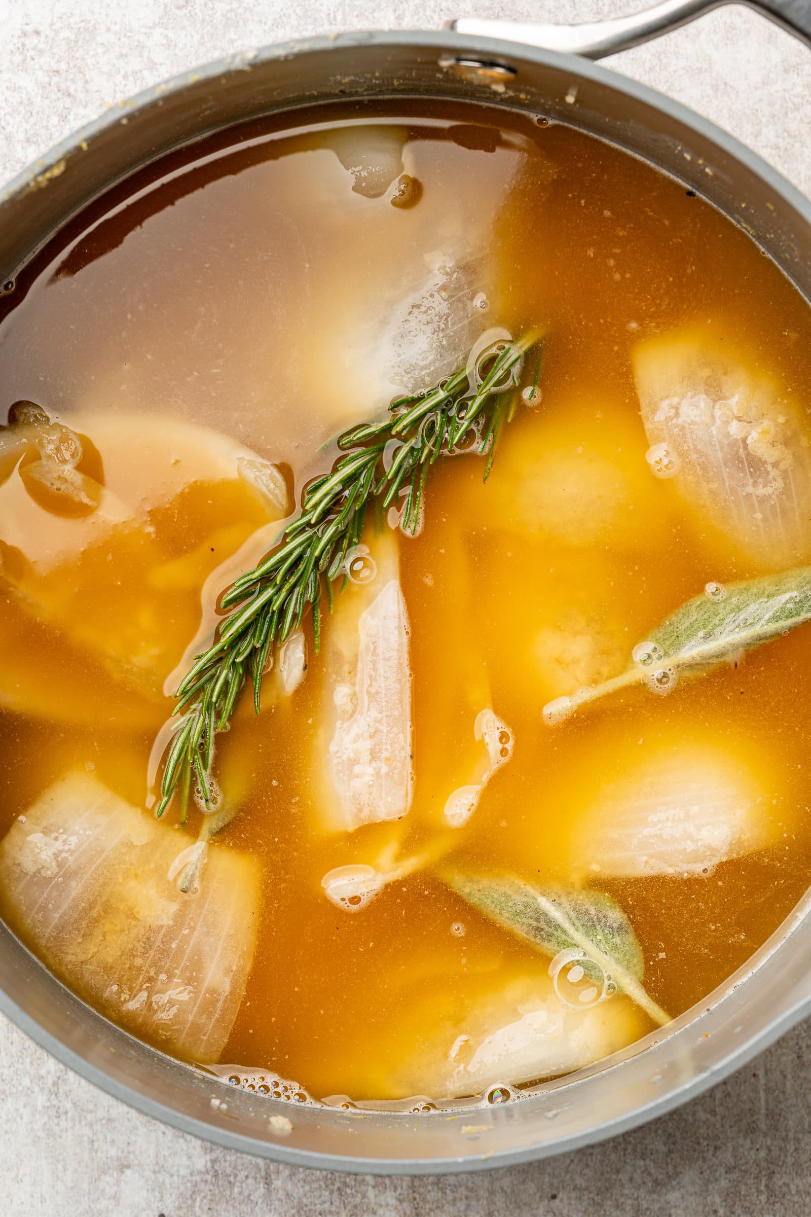 Vegetable broth poured over onions and herbs in pan.