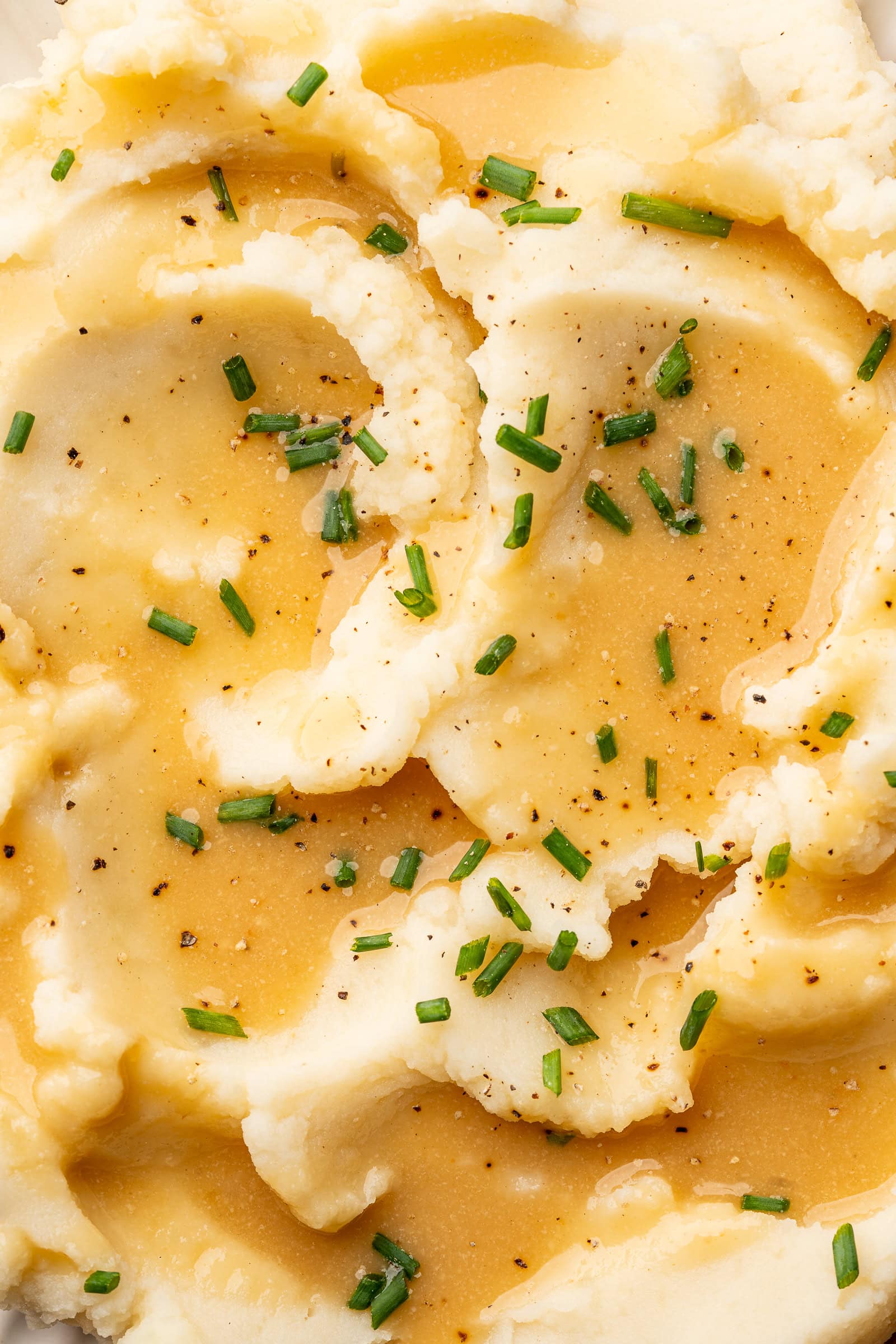 Close up of gravy spooned over mashed potatoes and garnished with chives.
