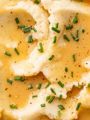 Close up of gravy spooned over mashed potatoes and garnished with chives.