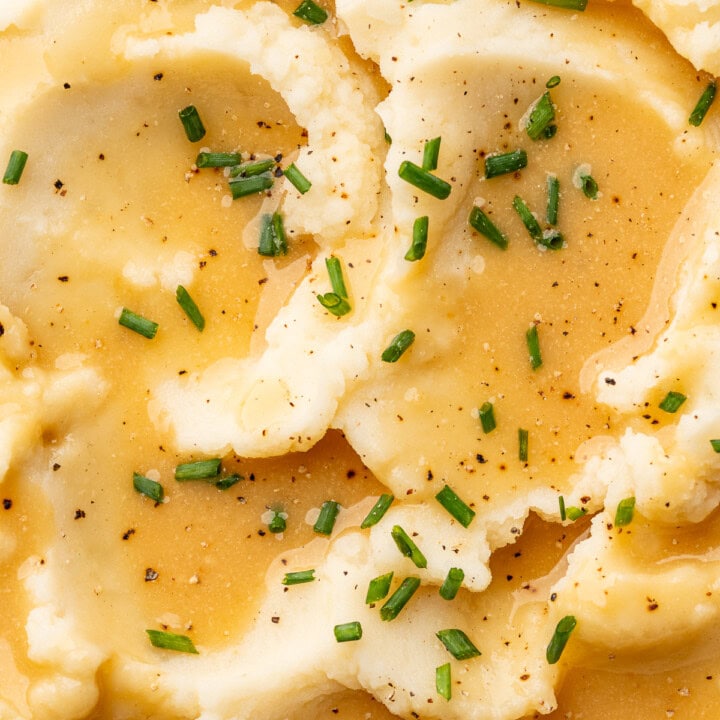 Close up of gravy spooned over mashed potatoes and garnished with chives.