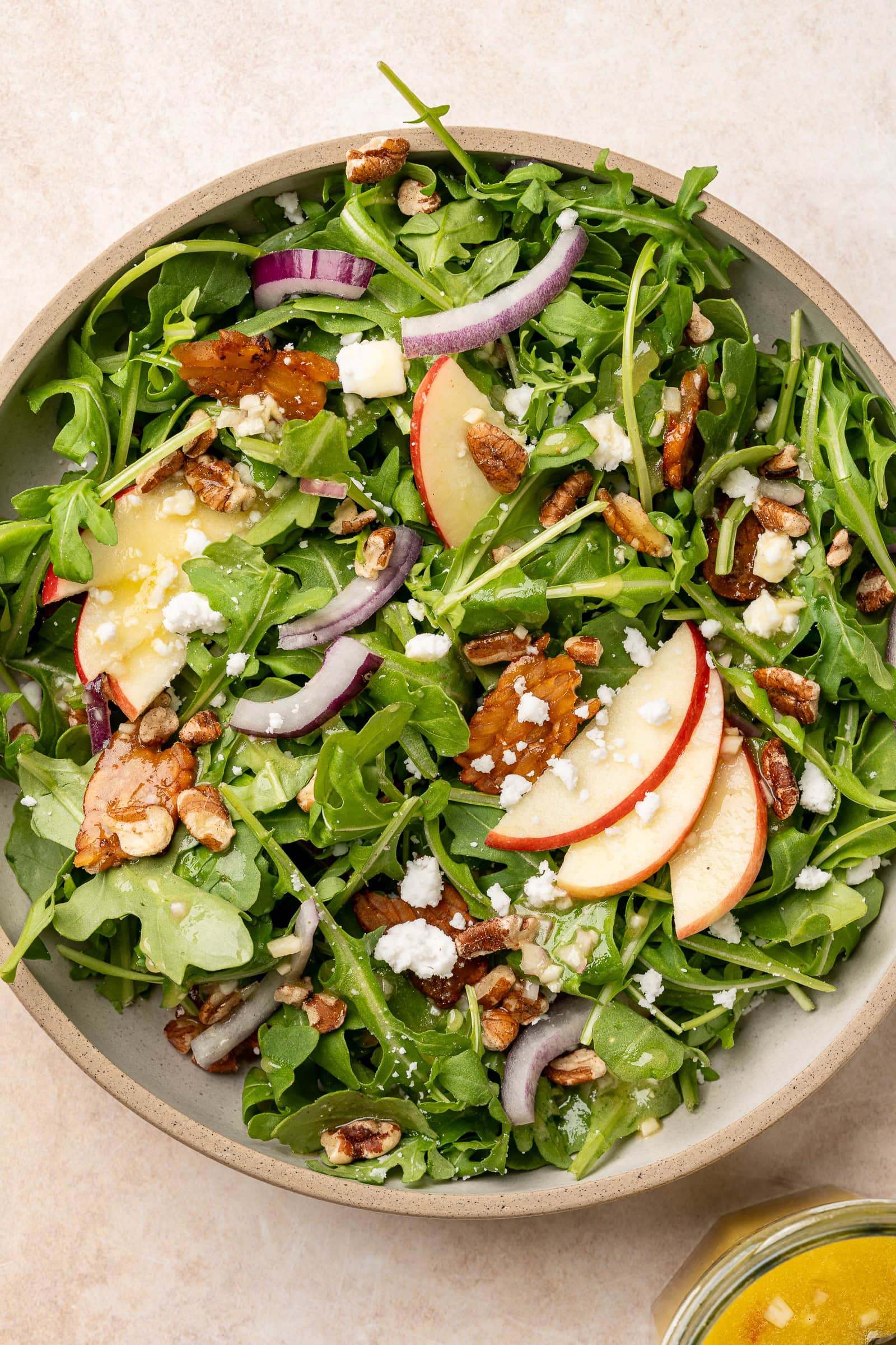 Apple arugula salad being dressed in a shallow bowl.