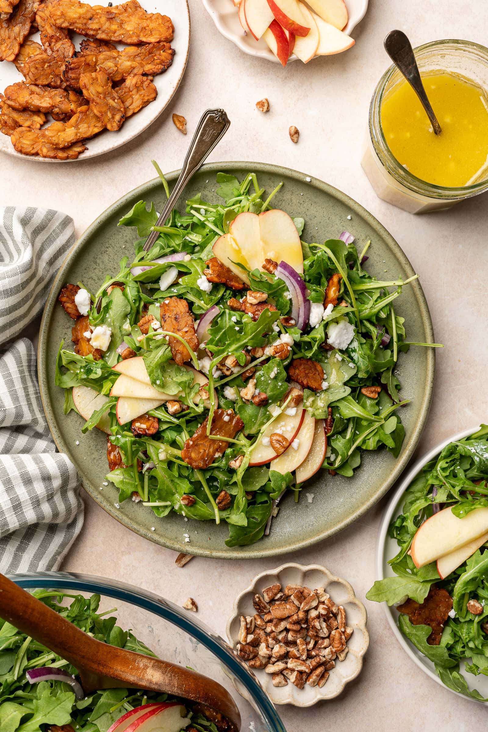 Apple arugula salad garnished with red onion, tempeh bacon, and vegan feta on a serving plate.