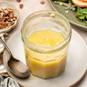 Apple cider vinaigrette in a jar surrounded by an apple salad and crushed pecans.