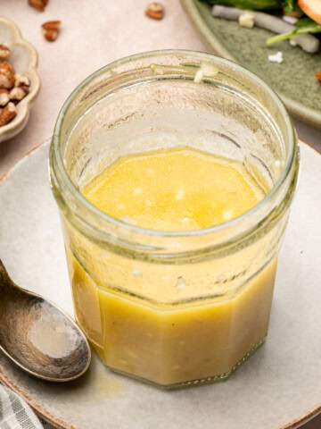 Apple cider vinaigrette in a jar surrounded by an apple salad and crushed pecans.