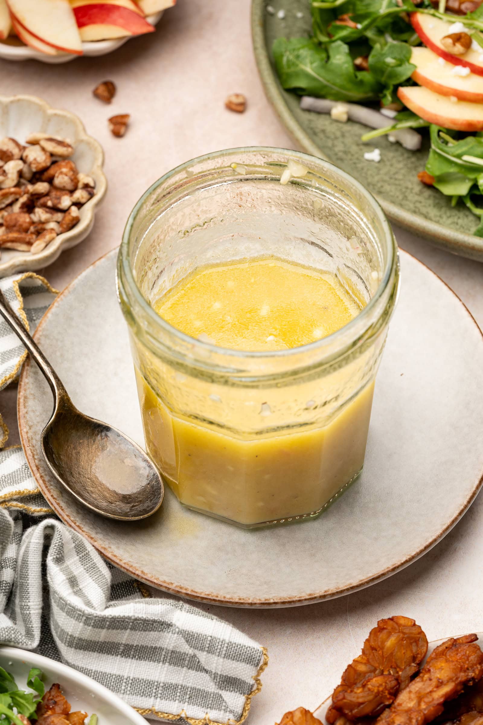 Apple cider vinaigrette in a jar surrounded by an apple salad and crushed pecans.