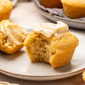 Cornbread muffin with a smear of maple butter with a bite taken out on a plate.