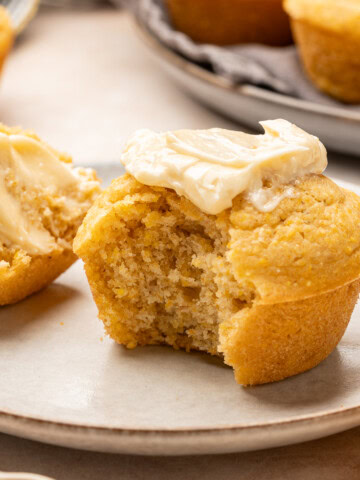 Cornbread muffin with a smear of maple butter with a bite taken out on a plate.