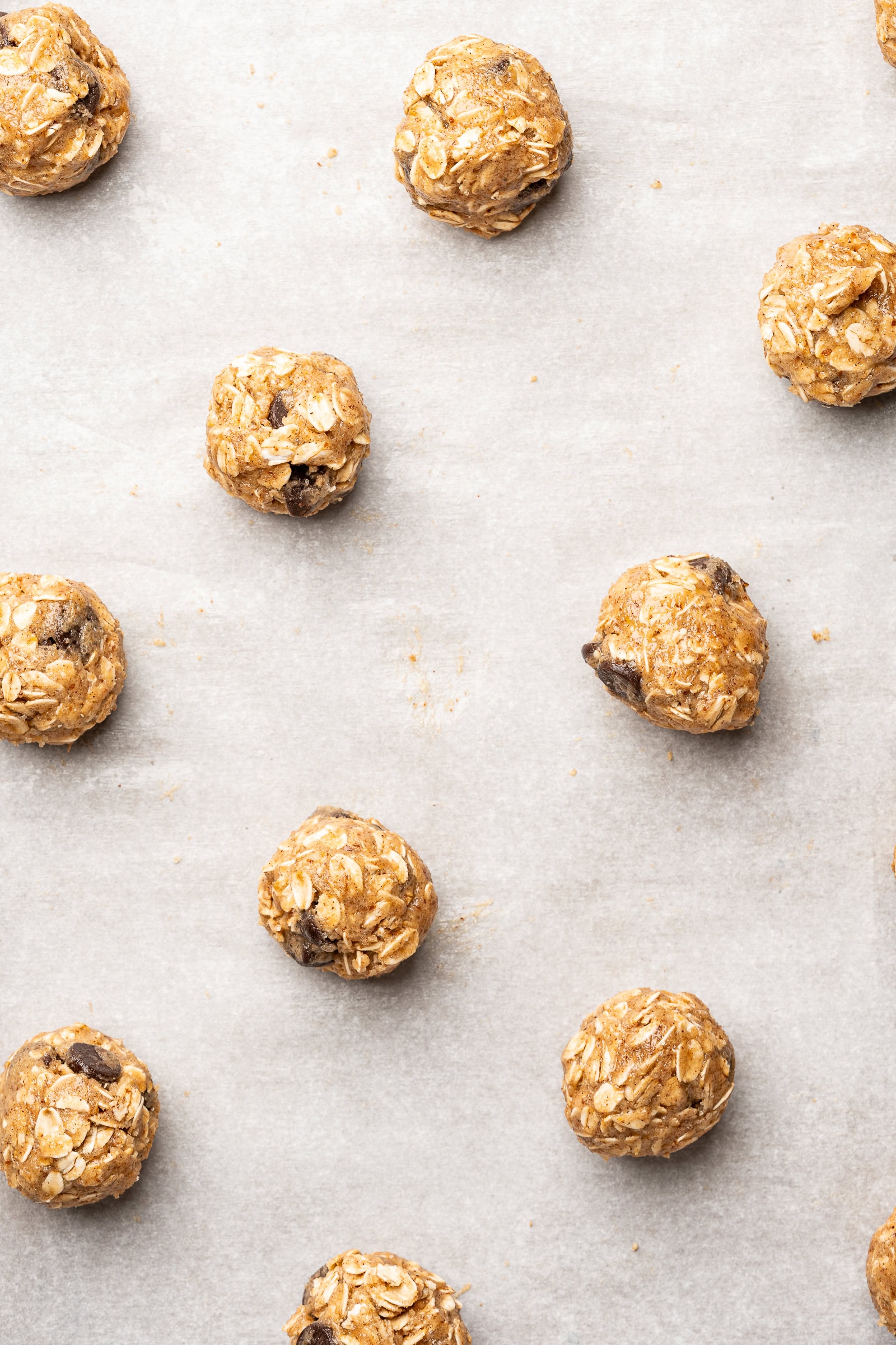 Oatmeal chocolate chip cookies spread a part on a parchment lined baking sheet before baking.