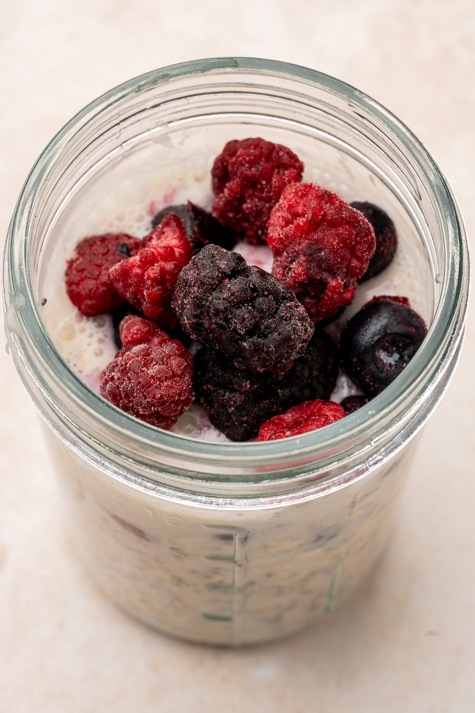 Overnight oats in a glass jar topped with frozen berries.