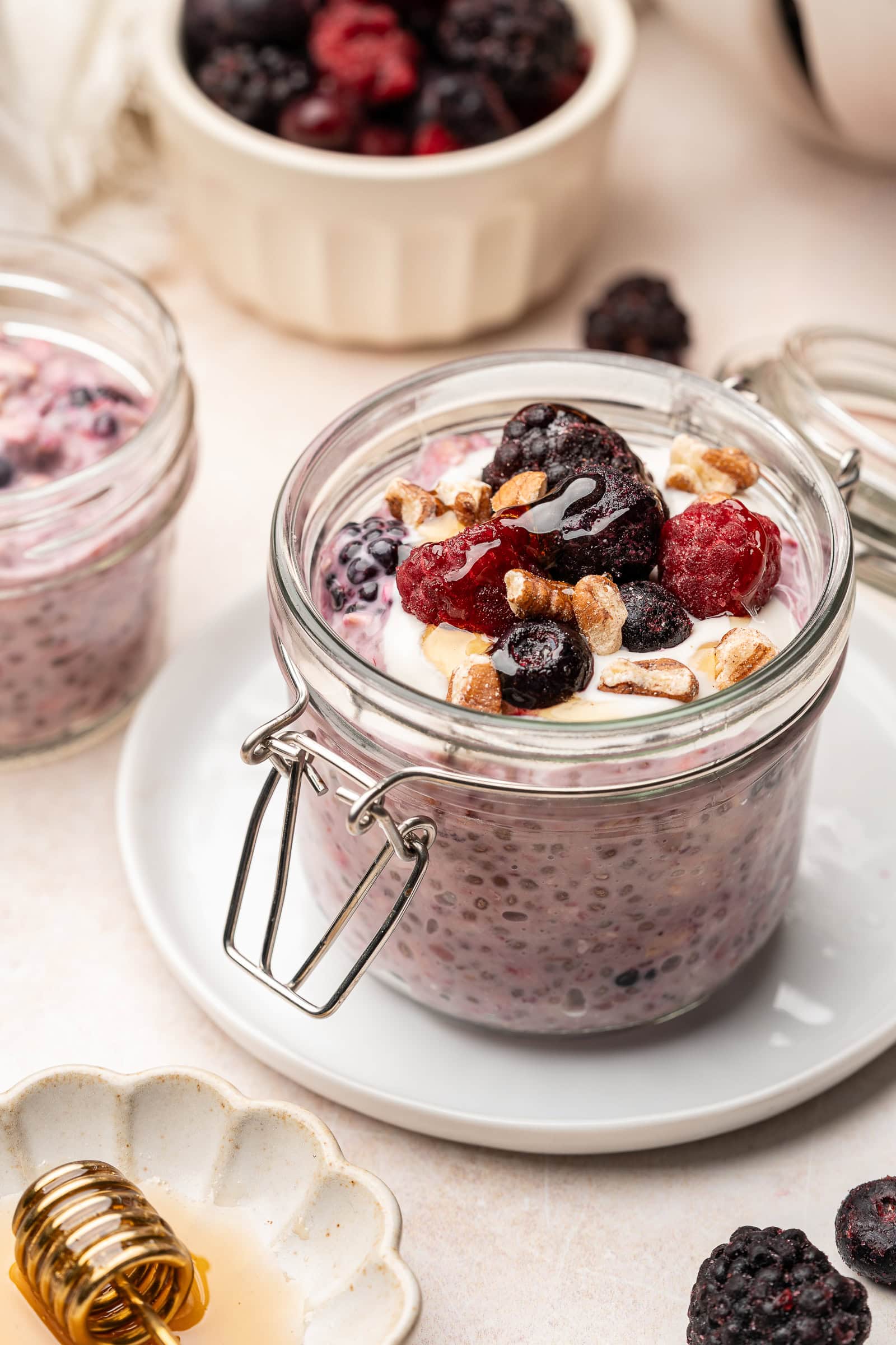 Berry overnight oats in serving jar topped with frozen fruit, yogurt, and chopped pecans.