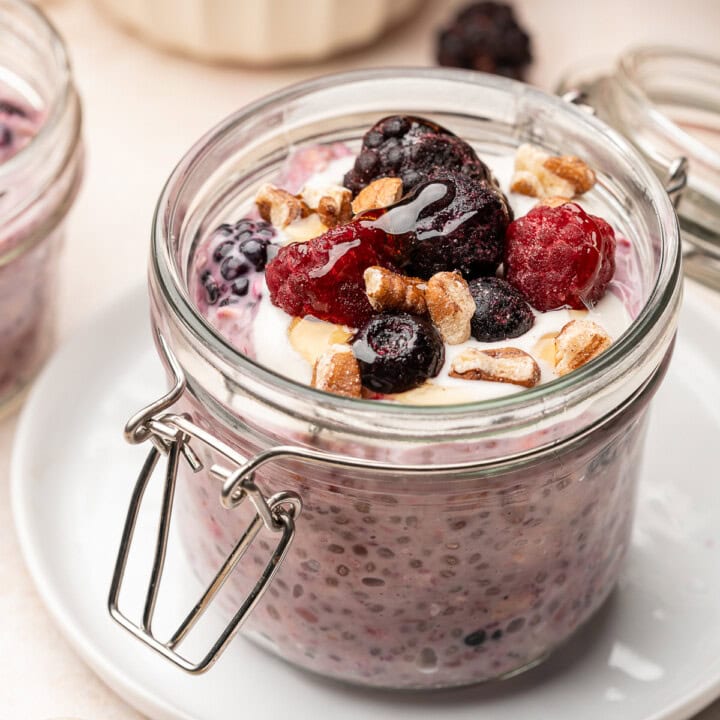 Berry overnight oats in serving jar topped with frozen fruit, yogurt, and chopped pecans.
