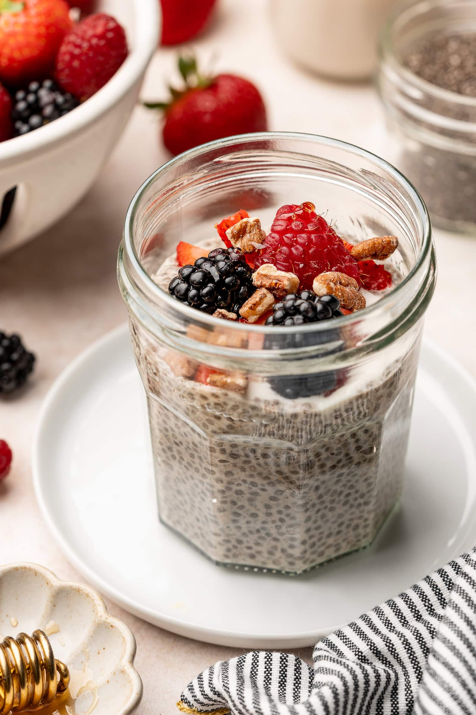 Oat milk chia pudding in a glass jar topped with berries and chopped pecans.