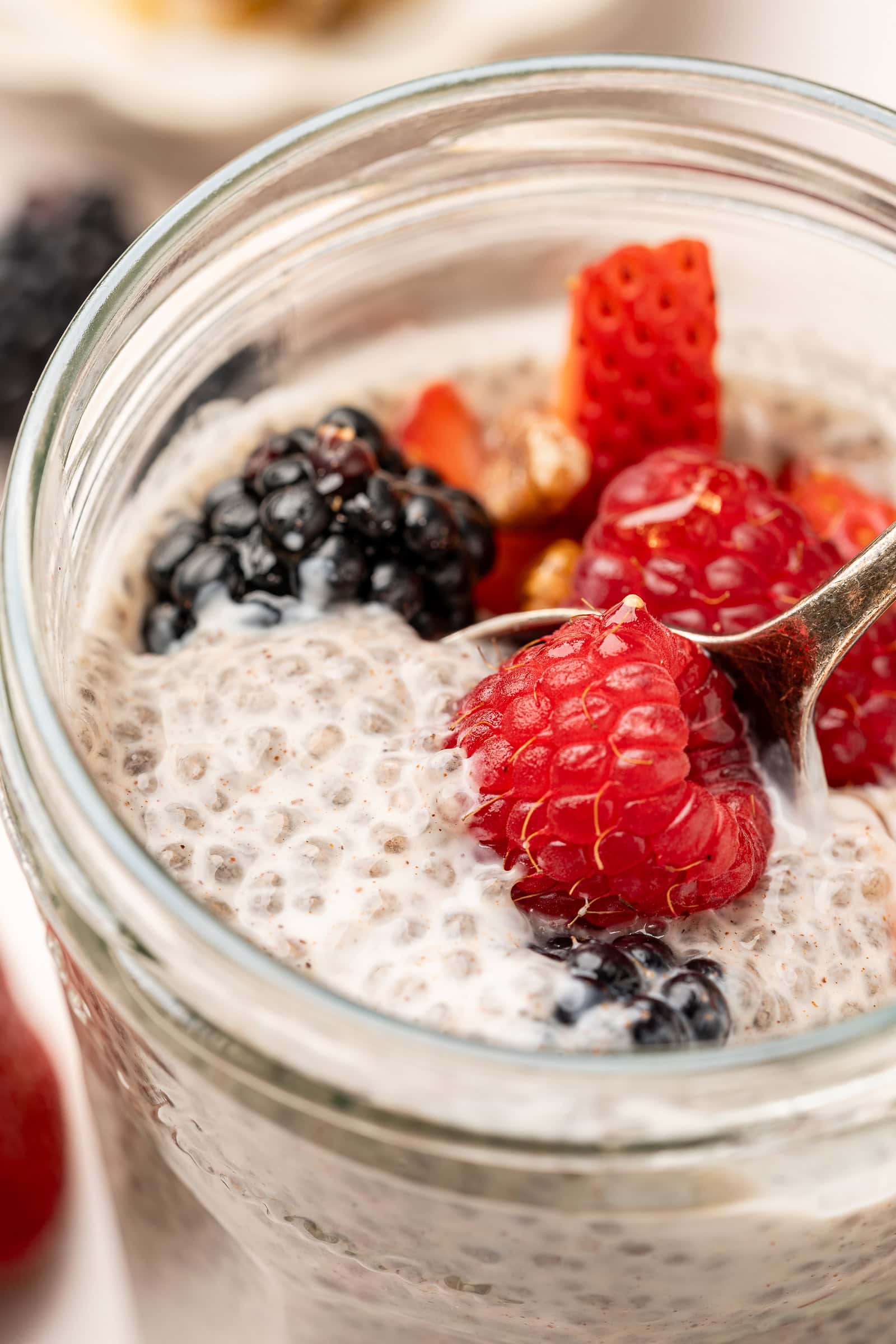 Close up of oat milk chia pudding in a glass jar topped with mixed berries.
