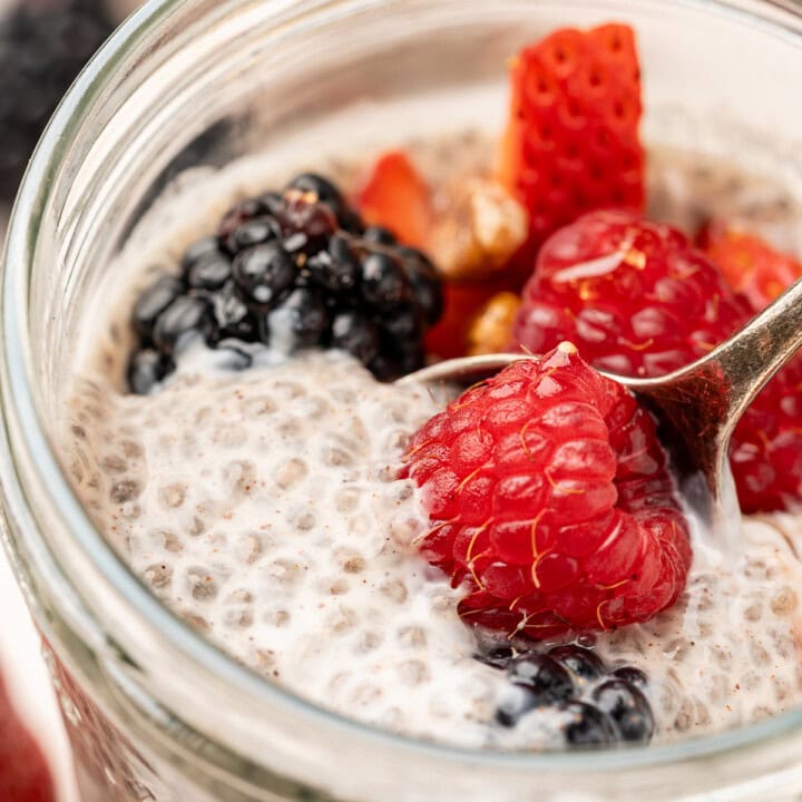 Close up of oat milk chia pudding in a glass jar topped with mixed berries.