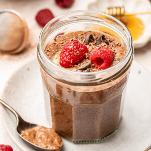 Chocolate chia pudding made with coconut milk in a glass jar and garnished with fresh raspberries, chocolate chips, and chocolate shavings.