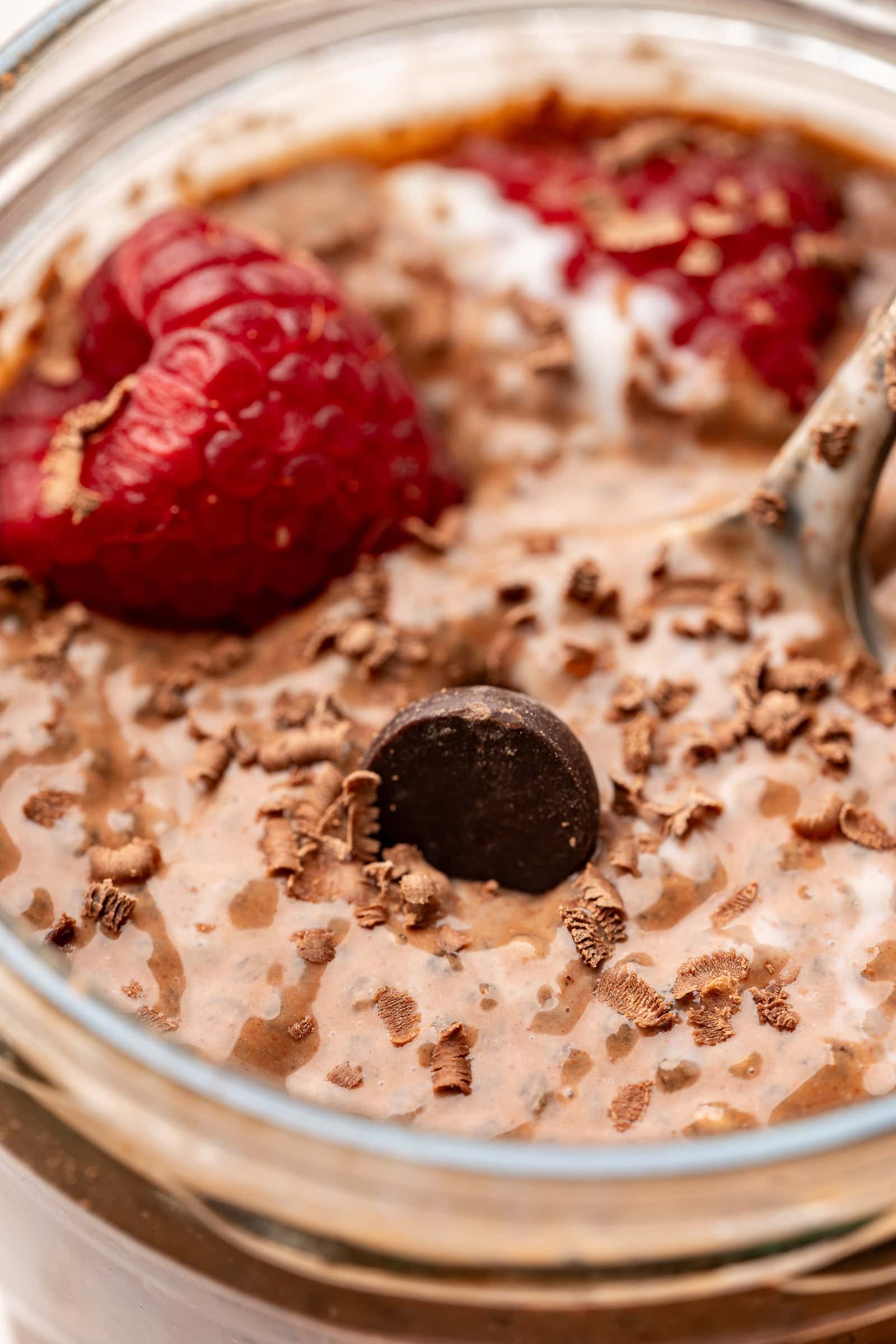Chocolate chia pudding made with coconut milk and garnished with chocolate shavings and raspberries in a glass jar.