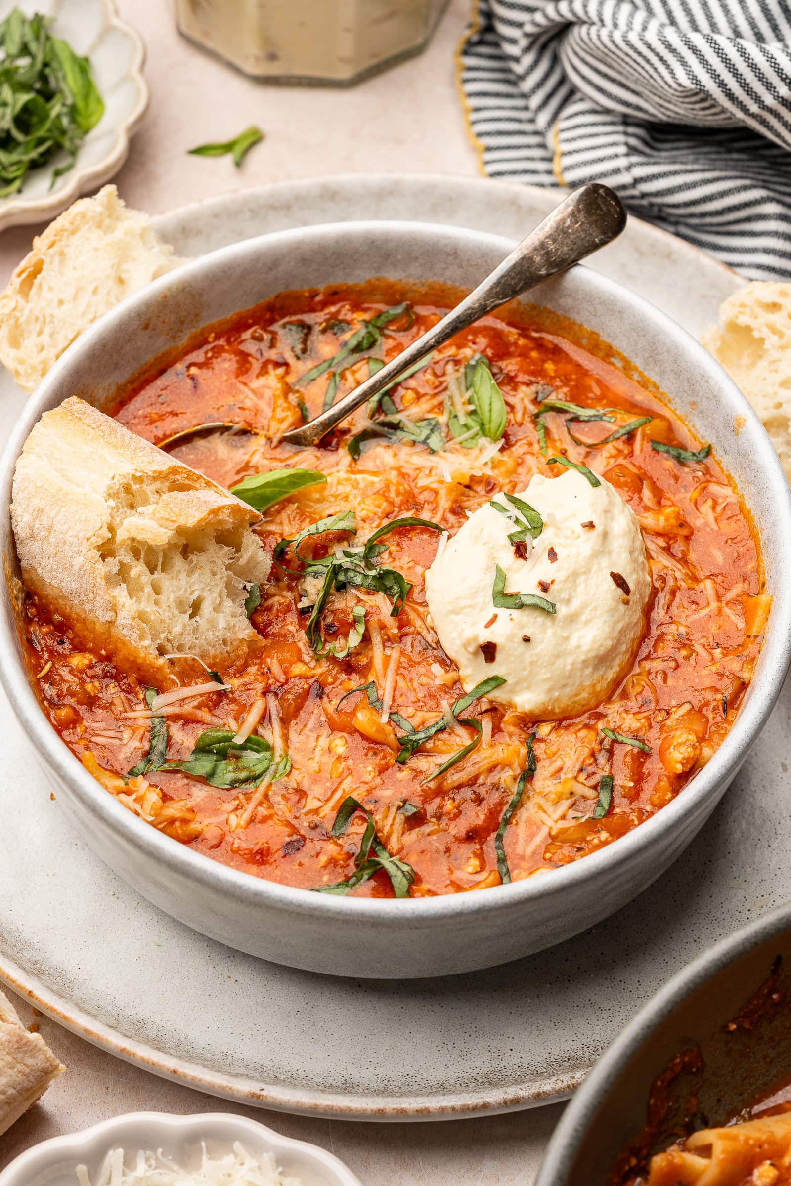 Lasagna soup in a serving bowl with vegan ricotta and garnished with basil and piece of bread.