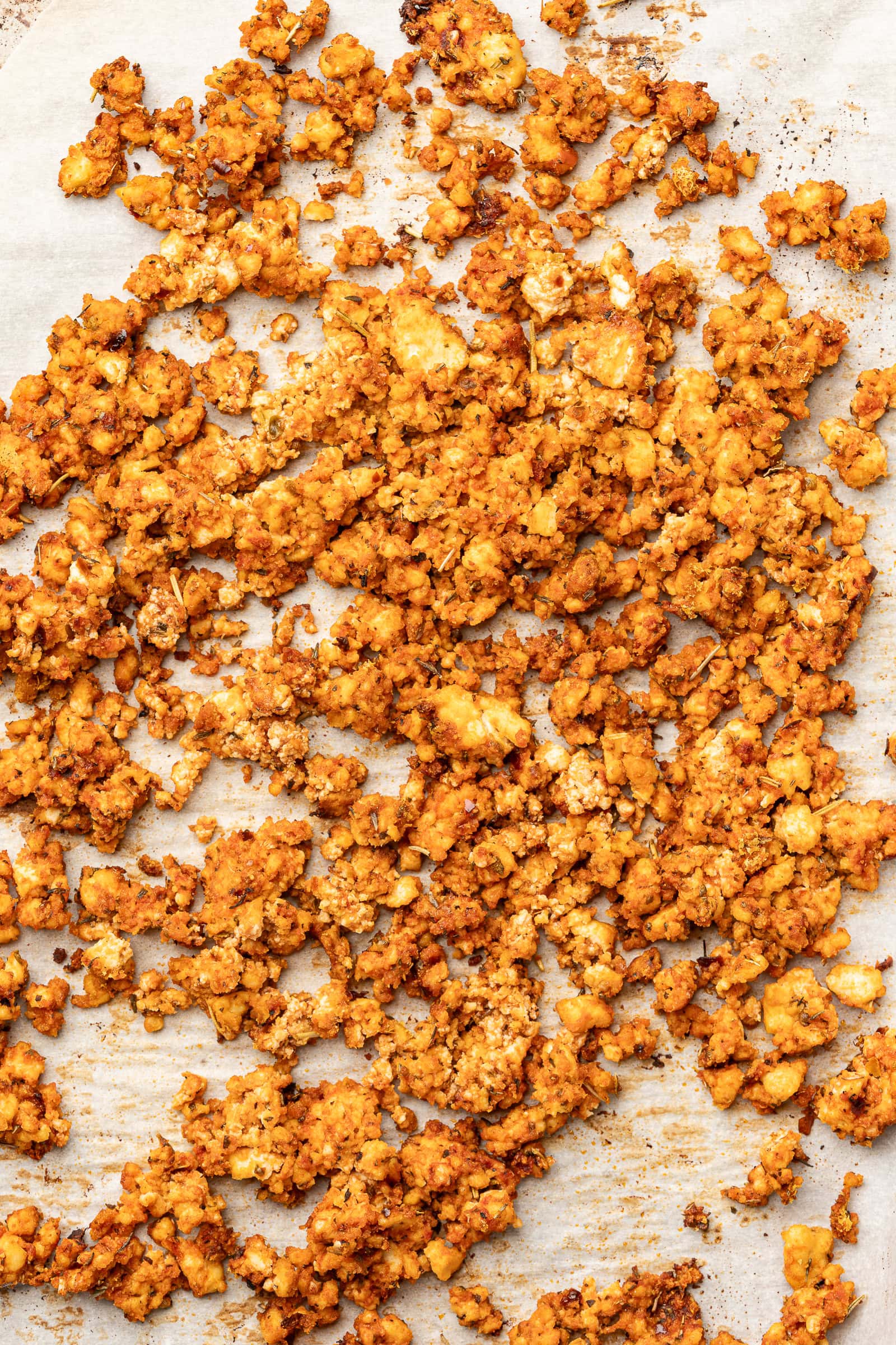 Baked and seasoned tofu crumbles on parchment lined baking sheet.
